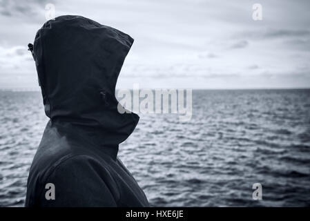 Personne à capuchon sans visage à la distance à l'horizon en plus de l'eau de mer sur journée d'hiver froides et venteuses, d'anticiper l'avenir imprévisible Banque D'Images