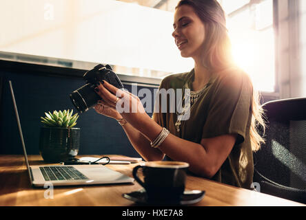 Young woman looking at camera while working on laptop. Le jeune photographe avec son appareil photo et ordinateur portable sur son bureau. Banque D'Images