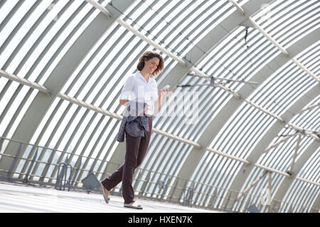 Side portrait of a smiling business woman walking and looking at mobile phone Banque D'Images