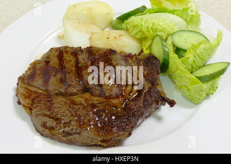 Un repas de grillades ou grillés ribeye steak servi avec des pommes de terre et une salade verte Banque D'Images