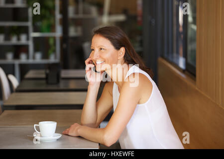 Portrait d'une femme dans son 30s talking on cell phone at a cafe Banque D'Images