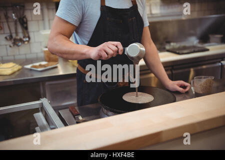 Portrait male chef pouring crêpe sur la poêle dans cuisine commerciale Banque D'Images