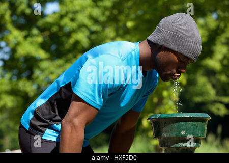 Portrait d'un côté jeune homme noir buvant à une fontaine à eau dans un parc public Banque D'Images