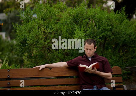 L'homme se détendre sur un banc de la lecture d'un livre. Banque D'Images