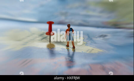 Focus sélectif de figurine miniature du jeune voyageur solitaire marche sur une grande carte avec broche rouge Banque D'Images