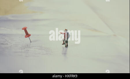 Focus sélectif de figurine miniature de lonely jeune voyageur avec sac à dos marche sur une grande carte avec broche rouge Banque D'Images