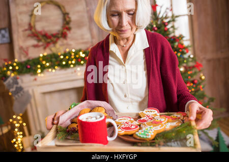 Smiling mature woman holding tray with christmas cookies et boisson chaude Banque D'Images