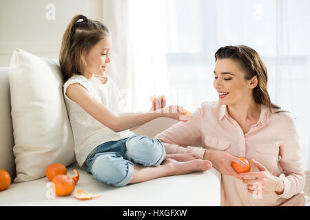 Mère et fille souriante de manger des mandarines à la maison Banque D'Images