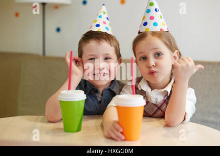 Adorable fille et garçon dans anniversaire-caps having drinks Banque D'Images