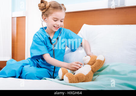 Portrait of smiling girl écoute infirmière teddy bear's heartbeat with stethoscope Banque D'Images