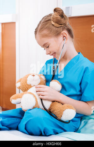 Portrait of smiling girl écoute infirmière teddy bear's heartbeat with stethoscope Banque D'Images