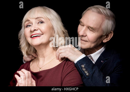 Smiling senior man putting golden collier autour du cou de happy woman on black Banque D'Images