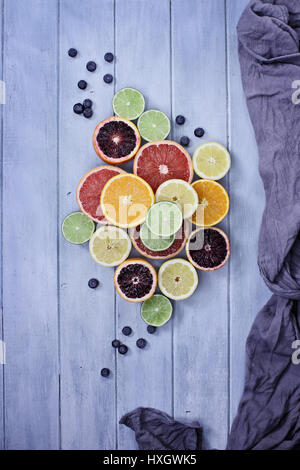 Variété d'agrumes (orange, oranges, citrons, pamplemousses, et limes) avec des bleuets avec tissu gris bleu sur une table rustique en bois haut. Banque D'Images