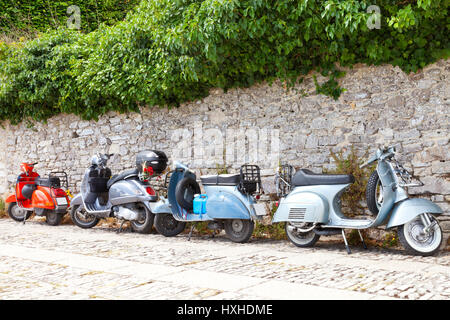 Erice, Sicile, Italie - 13 juin 2016 : rouge et bleu retro Vespa scooters italiens stationnés sur une route par un mur en pierre . Banque D'Images