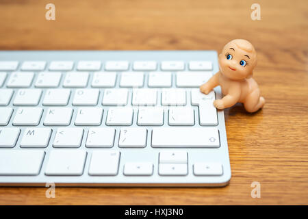 Photo Bande dessinée - little baby doll essaie de grimper sur le clavier, allongé sur une table en bois Banque D'Images