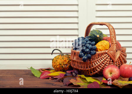 Citrouilles frais mûrs, de pommes et de raisins dans panier en osier sur fond de bois Banque D'Images