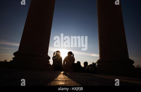 Munich, Allemagne. Mar 28, 2017. Les poussettes regarder le soleil se coucher entre les piliers de l'monopteros dans le Jardin Anglais de Munich, Allemagne, 28 mars 2017. Le monopteros, un temple construit dans un style grec, a été commandé par Leo von Klenze en 1836. Photo : Peter Kneffel/dpa/Alamy Live News Banque D'Images