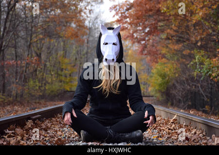 Femme assise sur les voies ferrées portant un masque de cheval Banque D'Images