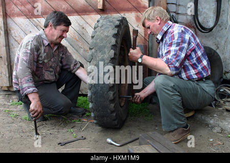 Lemozero, Olonets Karelia,, Russie - le 26 juillet 2006 : Deux agriculteurs mécanique auto, des pneus, dans la cour de l'atelier de réparation. Banque D'Images