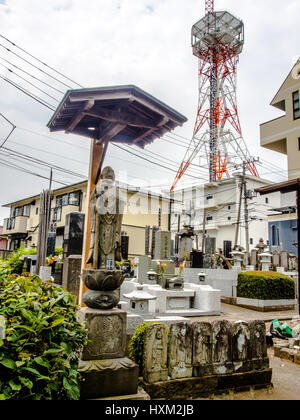 Statue bouddhiste et grave les décideurs à petit cimetière. Les immeubles à appartements et tour de communication à l'arrière-plan. Nishi Ward, Tokyo, Japon, Omiya Banque D'Images