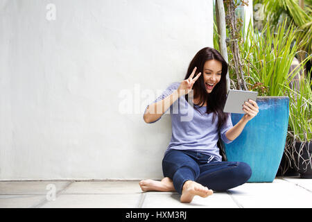 Portrait of smiling young woman sitting on floor faisant appel vidéo using digital tablet Banque D'Images