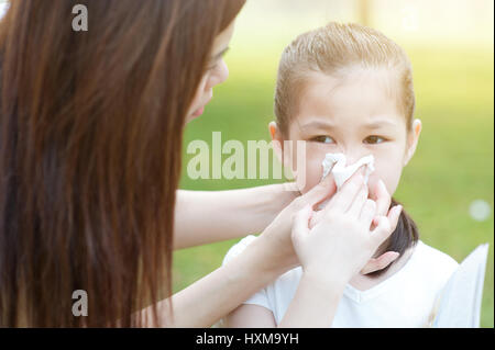 L'allergie. Mère et little girl blowing nez à l'extérieur, dans le parc. Famille vie de plein air. Banque D'Images