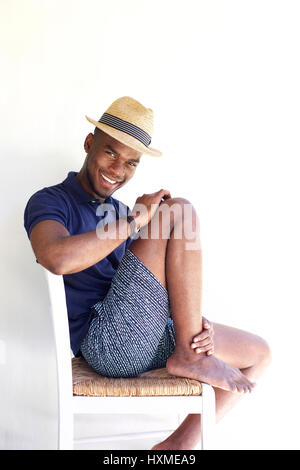 Portrait de jeune homme élégant assis sur une chaise et smiling against white background Banque D'Images