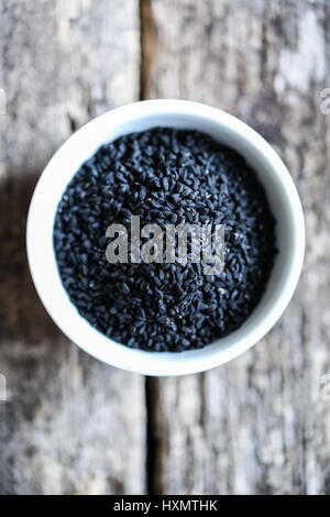 Les graines de cumin noir dans un bol blanc sur une table en bois Banque D'Images