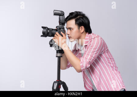 Vue latérale du jeune photographe asiatique tenant un appareil photo numérique, tout en travaillant en studio Banque D'Images