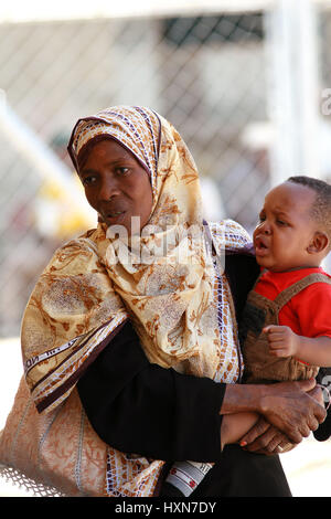 Zanzibar, Tanzanie - le 16 février 2008 : femme tanzanienne avec sa tête couverte d'un grand mouchoir à motifs, tenant dans ses bras, un enfant et un Banque D'Images