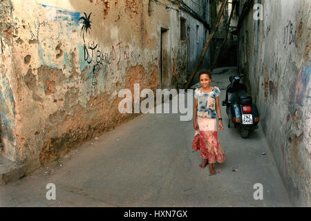 Zanzibar, Tanzanie - le 16 février 2008 : La fille de l'Afrique de l'inconnu d'environ 10 ans, debout près du mur peint de vieilles maisons en pierre en ruine. Banque D'Images