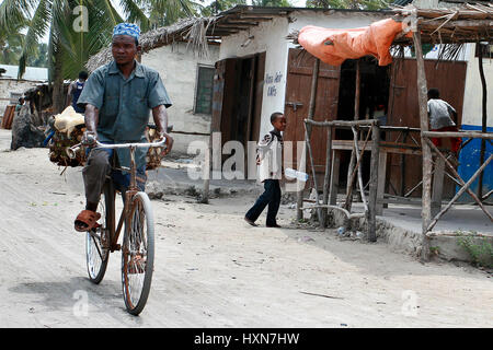 Zanzibar, Tanzanie - Février 18, 2008 : l'Afrique noire inconnue des hommes dans les Etats arabes skullcap, rouler à vélo sur une rue poussiéreuse dans la ville de pêche. Banque D'Images