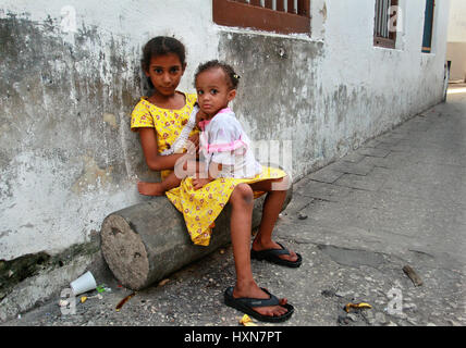 Zanzibar, Tanzanie - le 16 février 2008 : la Tanzanie, Zanzibar, Stone Town, une petite fille africaine à la peau sombre 8 ans, assis sur un rondin près de la maison Banque D'Images