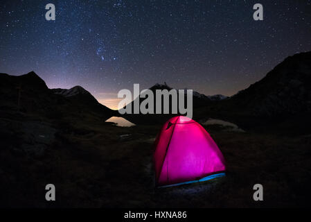 Le camping sous un ciel étoilé et la Voie Lactée arc à haute altitude sur les Alpes italiennes. Tente rougeoyante au premier plan. Aventure dans la nature. Banque D'Images