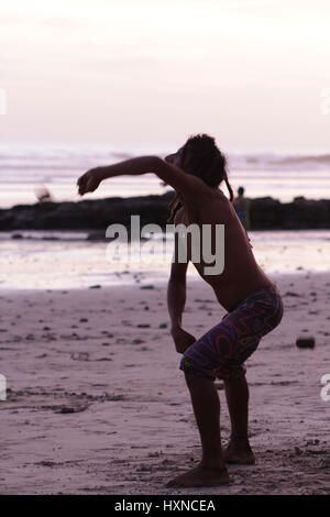 Un homme danse sur la plage pendant le coucher du soleil Banque D'Images