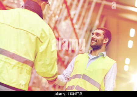 Les hommes dans les gilets de sécurité shaking hands at warehouse Banque D'Images