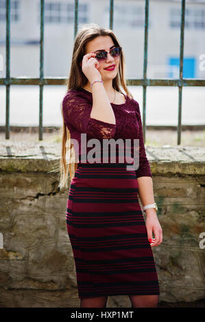 Jeune adolescente chubby usure sur robe rouge avec des lunettes posées contre clôture de fer. Banque D'Images