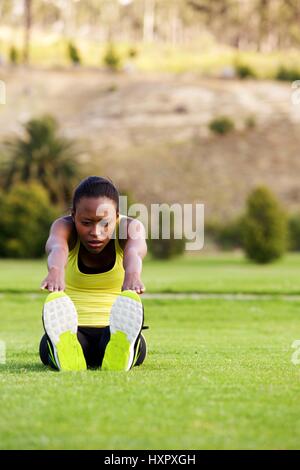 Portrait de jeune femme africaine faisant exercice s'étendant sur l'herbe verte du park Banque D'Images
