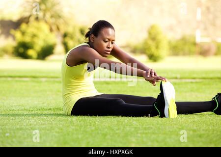Portrait of young African woman sitting on grass s'étendant jusqu'à atteindre les orteils Banque D'Images