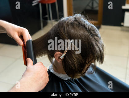 Coiffure masculine se prépare à décote de belle femme dans le salon de beauté. Il se redresse les cheveux. Banque D'Images