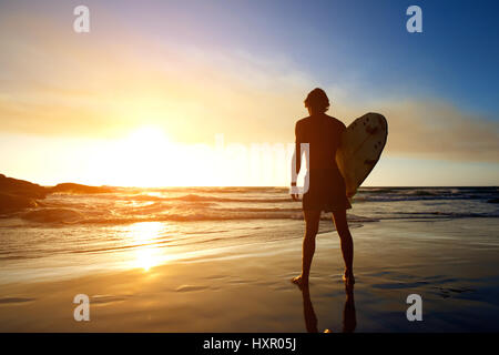 Portrait de dos de surfer regardant le coucher du soleil sur la plage Banque D'Images