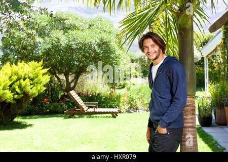 Portrait of happy young man standing against tree in backyard Banque D'Images