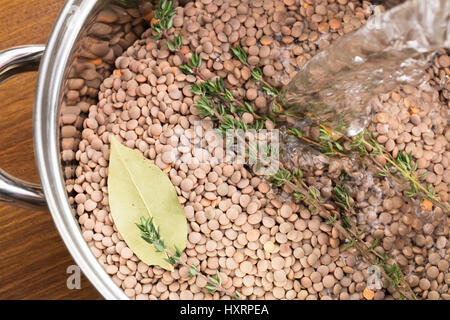 L'eau est versée dans le pot des lentilles et des herbes pour faire de la soupe Banque D'Images