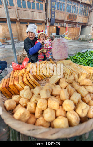 Zhaoxing Village Dong, province de Guizhou, Chine - 8 Avril 2010 : Rue du commerce dans la campagne d'Asie, une vieille femme tenant un enfant, vend fried Banque D'Images