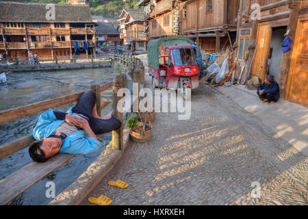 Zhaoxing Village Dong, province de Guizhou, Chine - 8 Avril 2010 : Jeune homme de dormir sur un banc au milieu de village des minorités ethniques, entouré Banque D'Images