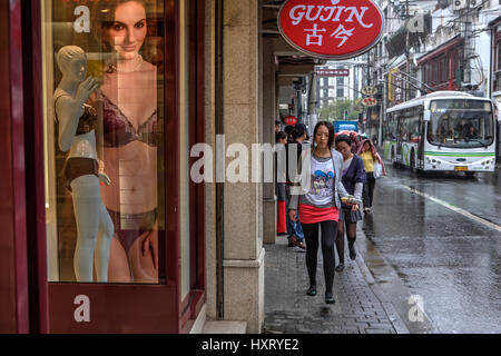 Shanghai, Chine - le 20 avril 2010 : les passants sur la chaussée mouillée, en passant par la boutique sur une rue de la ville. Asian girl dans une courte jupe rouge, col Banque D'Images