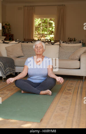 Serene woman méditant dans la position du lotus à la maison Banque D'Images