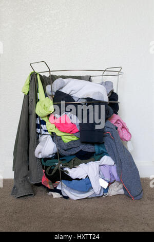 Panier à linge en métal coloré plein de vêtements sales contre mur blanc, sur fond de tapis marron Banque D'Images