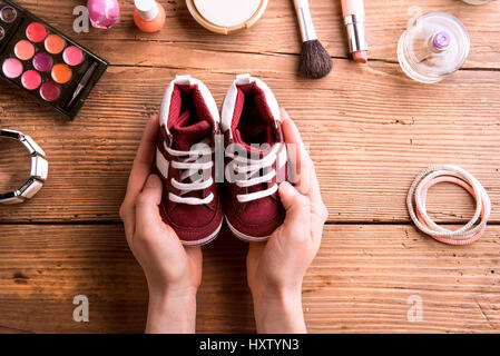 La Fête des mères, la composition. Mains de méconnaissable woman holding peu chaussures pour enfants. Divers produits de beauté mis sur table. Studio shot sur ba en bois Banque D'Images