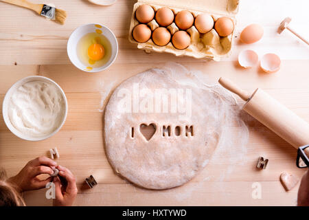 La fête des Mères, la composition. Mains de méconnaissable girl baking cookies, jouer avec la pâte. J'aime Maman signe fait avec des emporte-pièce. Studio shot sur bois Banque D'Images